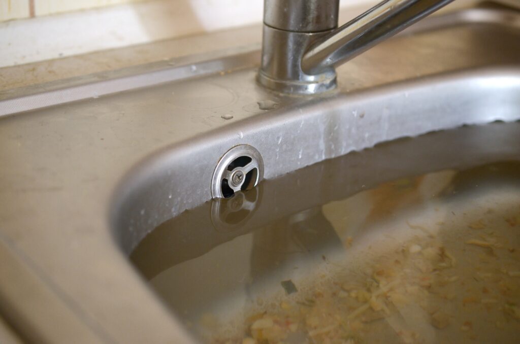 Stainless steel sink plug hole close up full of water and particles of food